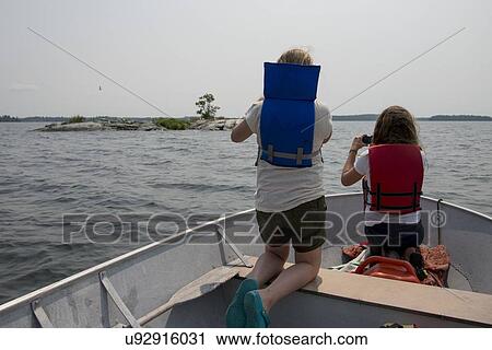 Stock Image - Girls sitting in a boat and looking through binoculars, Lake of The Woods, Keewatin, Ontario, Canada. Fotosearch