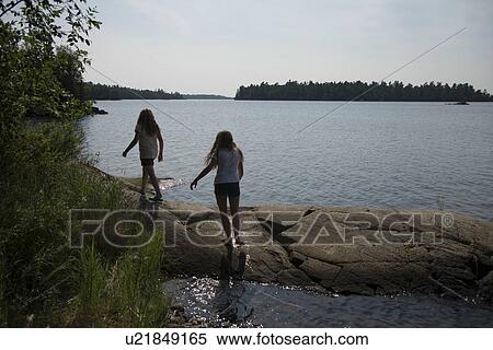 Stock Photography - Girls walking on the rocks at the lakeside, Lake of The Woods, Kenora, Unorganized Kenora, Ontario, Canada. Fotosearch