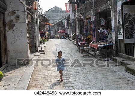 Stock Image - Little girl walking on a street, Xingping, Yangshuo, Guilin, Guangxi Province, China. Fotosearch