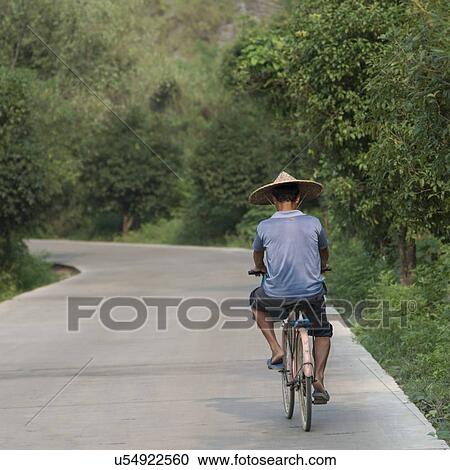 Stock Image - Man cycling on the road, Yangshuo, Guilin, Guangxi Province, China. Fotosearch