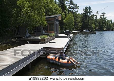 Stock Image - Man sitting on an inflatable raft floating in a lake, Lake of The Woods, Ontario, Canada. Fotosearch