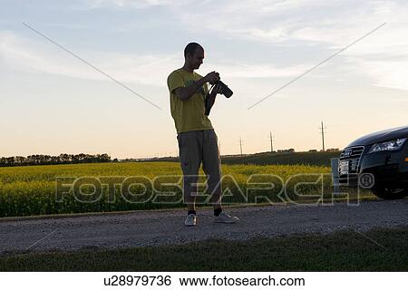 Stock Photograph - Photographer standing on the road and adjusting his camera, Manitoba, Canada. Fotosearch