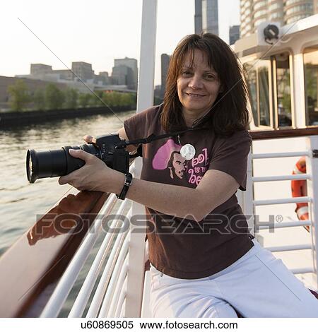 Stock Photography - Portrait of a woman sitting in a boat holding a digital camera, Lake Michigan, Chicago, Cook County, Illinois, USA. Fotosearch