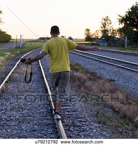 Stock Image - Rear view of a man balancing on a railroad track, Manitoba, Canada. Fotosearch