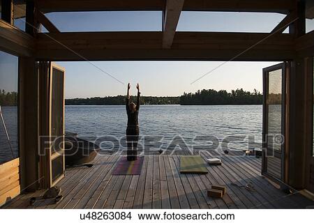 Picture - Rear view of a person practicing yoga on a pier, Lake of The Woods, Ontario, Canada. Fotosearch