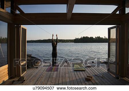 Stock Photo - Rear view of a person practicing yoga on a pier, Lake of The Woods, Ontario, Canada. Fotosearch