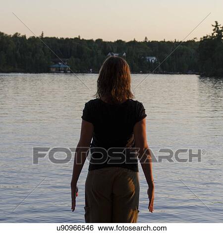 Stock Photograph - Rear view of a woman looking at lake view, Lake of The Woods, Keewatin, Ontario, Canada. Fotosearch