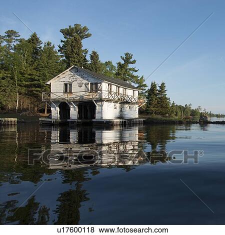 Stock Photo - Reflection of a boat house and shoreline, Lake of The Woods, Ontario, Canada. Fotosearch
