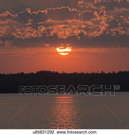 Stock Image - Reflection of sun as it sets, Lake of The Woods, Ontario, Canada. Fotosearch