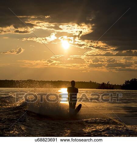 Stock Image - Silhouette of a person waterskiing in a lake at dusk, Lake of The Woods, Keewatin, Ontario, Canada. Fotosearch