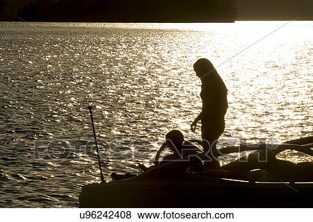 Stock Photo - Silhouette of two people on a motorboat at sunset, Lake of The Woods, Keewatin, Ontario, Canada. Fotosearch