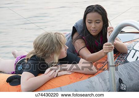 Stock Image - Two girls enjoying on inflatable raft in the lake, Lake Of The Woods, Keewatin, Ontario, Canada. Fotosearch