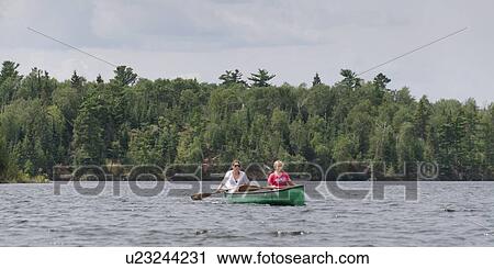 Stock Image - Two girls rowing a boat in a lake, Lake of The Woods, Ontario, Canada. Fotosearch