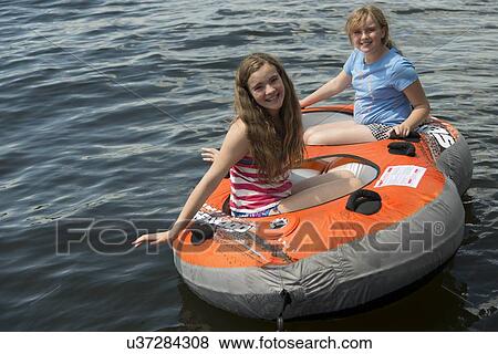 Stock Photo - Two girls sitting on an inflatable raft floating in a lake, Lake of The Woods, Ontario, Canada. Fotosearch