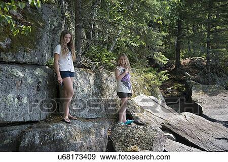 Stock Photo - Two girls standing on rocks in a forest, Kenora, Lake of The Woods, Ontario, Canada. Fotosearch
