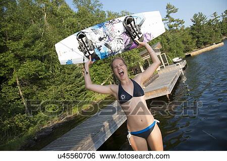 Stock Photograph - Woman holding a wakeboard and looking excited at the lakeside, Lake of The Woods, Keewatin, Ontario, Canada. Fotosearch
