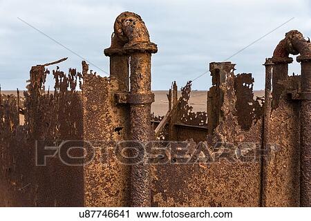 Stock Image - Abandoned rusty oil rig on Skeleton Coast, detail of pipes and jagged edges, with sea and sky beyond, Namibia, South West Africa. Fotosearch