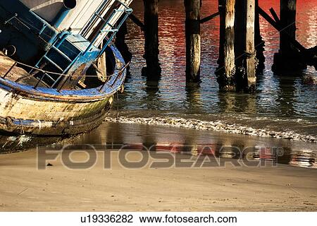 Abandoned wooden boat with peeling blue paint lying on one side at sea water edge, wooden pillars of pier beyond, and red reflection in water, Luderitz, Namibia, South West Africa View Large Photo Image Stock Image - Abandoned wooden boat with peeling blue paint lying on one side at sea water edge, wooden pillars of pier beyond, and red reflection in water, Luderitz, Namibia, South West Africa. Fotosearch