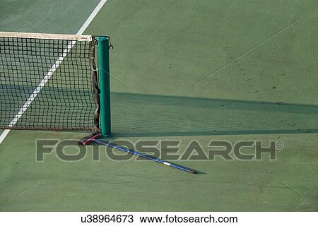 Stock Image - Aerial view of green tennis court, close up detail showing part of net, net shadow, white marker lines, and sweeping brush lying on the court, at athletic centre, in early morning sunshine, Todi, Umbria, Italy. Fotosearch