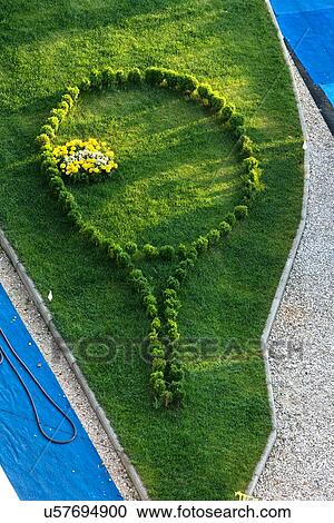 Stock Image - Aerial view of lawn with bushes planted in outline of a tennis racquet, and yellow flowers within to represent tennis ball, at athletic centre, in early morning sunshine, Todi, Umbria, Italy. Fotosearch