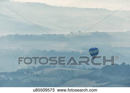 Aerial view of layered hills of the Middle Tiber Valley in early morning hazy sunshine, with a hot air balloon floating above, Todi, Umbria, Italy View Large Photo Image Stock Image - Aerial view of layered hills of the Middle Tiber Valley in early morning hazy sunshine, with a hot air balloon floating above, Todi, Umbria, Italy. Fotosearch