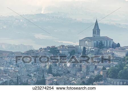 Picture - Aerial view of medieval city of Todi with church and spire of San Fortunato church and layered hills of the Middle Tiber Valley beyond, in early morning hazy sunshine, Todi, Umbria, Italy. Fotosearch