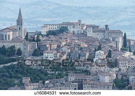 Stock Image - Aerial view of medieval city of Todi with church and spire of San Fortunato church on left, and Duomo and Piazza del Popolo on right, in early morning sunshine, Todi, Umbria, Italy. Fotosearch