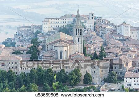Stock Photography - Aerial view of medieval city of Todi with church and spire of San Fortunato church in foreground, and Duomo and Piazza del Popolo beyond, in early morning hazy sunshine, Todi, Umbria, Italy. Fotosearch