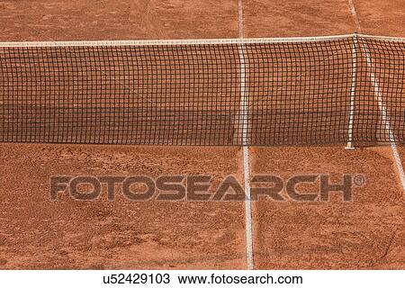 Stock Image - Aerial view of red clay tennis court, close up detail showing part of net and painted lines, creating geometric pattern at athletic centre, in early morning sunshine, Todi, Umbria, Italy. Fotosearch