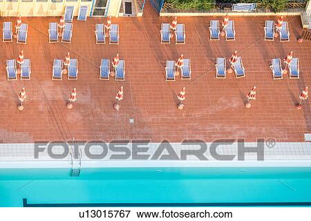 Aerial View Of Swimming Pool Blue Deck Chairs In Pairs On Red Tiles With Closed Umbrellas Creating Geometric Pattern Close Up Early Morning Aerial View Of Swimming Pool Blue Deck Chairs In Pairs On Red Tiles With Closed Umbrellas Creating Geometric Pattern Close Up Early Morning