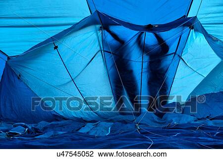 Stock Image - Close up of interior of blue and navy blue hot air balloon envelope being inflated with silhouettes of two people working with arms raised on the outside, Todi Mongolfiere Hot Air Balloon Festival, Italy. Fotosearch