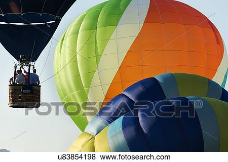 Close up of multicoloured hot air balloons inflated and about to launch with another colourful balloon in blue sky above, Todi Mongolfiere Hot Air Balloon Festival, Umbria, Italy View Large Photo Image Stock Photo - Close up of multicoloured hot air balloons inflated and about to launch with another colourful balloon in blue sky above, Todi Mongolfiere Hot Air Balloon Festival, Umbria, Italy. Fotosearch