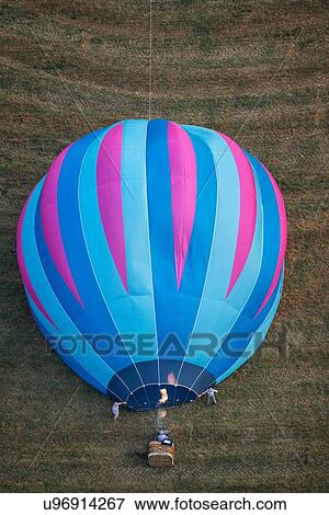 Stock Photo - Close up of multicoloured hot air balloons inflating, held by two men as flame is heating envelope, seen from air, Todi Mongolfiere Hot Air Balloon Festival, Umbria, Italy. Fotosearch