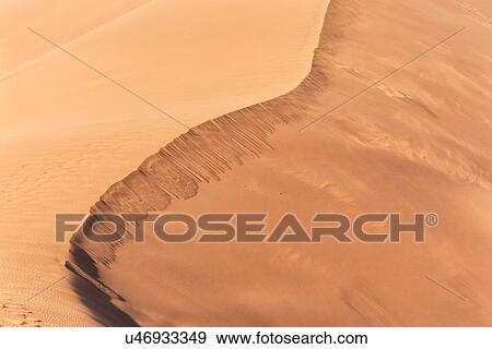 Stock Photo - Close up view of line of red sand dune with different tones in shadow of early morning sunlight, and sand being blown by winds, Namib desert, Namibia, South West Africa. Fotosearch