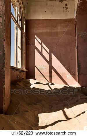 Stock Image - Kolmanskop interior view of room: pink painted walls, broken window creating shadows, sand dune which fills the room, abandoned German mining town, Namib desert, Namibia, South West Africa. Fotosearch