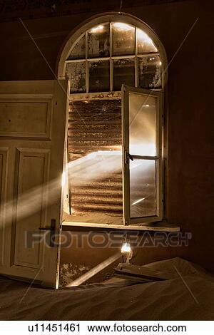 Stock Image - Kolmanskop interior view of room: window open with opaque glass, rusty shutters with rays of sunlight streaming through cracks, detail view, abandoned German mining town, Namib desert, Namibia, South West Africa. Fotosearch