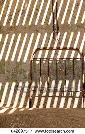 Kolmanskop interior view of room: detail of wall shadows created by roof slats, and metal bed frame with slat pattern propped against wall, abandoned German mining town, Namib desert, Namibia, South West Africa View Large Photo Image Stock Photo - Kolmanskop interior view of room: detail of wall shadows created by roof slats, and metal bed frame with slat pattern propped against wall, abandoned German mining town, Namib desert, Namibia, South West Africa. Fotosearch
