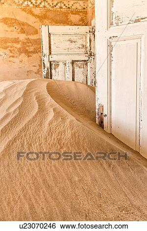 Stock Photograph - Kolmanskop interior view of room: doorway with orange painted walls and stencilling, leading to other rooms and sand dune which fills the room, abandoned German mining town, Namib desert, Namibia, South West Africa. Fotosearch