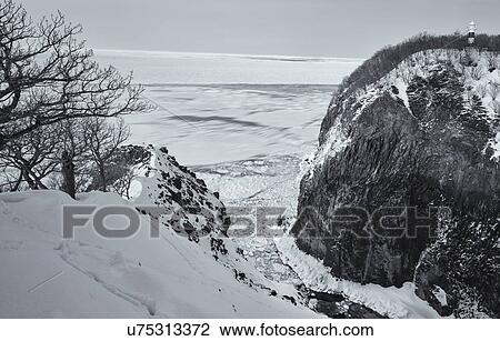 Monochrome aerial view of floating sea ice in a channel: deep gully with steep cliffs either side in the snow, lighthouse on top, with open sea beyond, Shiretoko National Park, Hokkaido, Japan View Large Photo Image Stock Image - Monochrome aerial view of floating sea ice in a channel: deep gully with steep cliffs either side in the snow, lighthouse on top, with open sea beyond, Shiretoko National Park, Hokkaido, Japan. Fotosearch