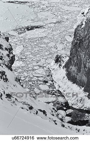 Stock Photograph - Monochrome aerial view of floating sea ice in a channel: deep gully with steep cliffs either side in the snow, Shiretoko National Park, Hokkaido, Japan. Fotosearch