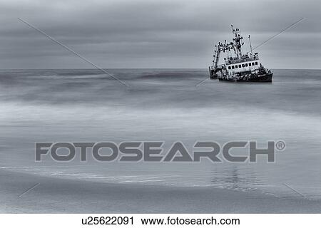 Old fishing boat run aground in shallow water off Skeleton Coast: twilight with motion blur of waves splashing, monochrome image, Namibia, South West Africa View Large Photo Image Stock Image - Old fishing boat run aground in shallow water off Skeleton Coast: twilight with motion blur of waves splashing, monochrome image, Namibia, South West Africa. Fotosearch