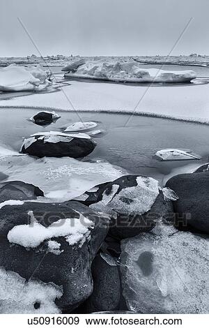 Rocks covered with snow at water's edge, ice patches forming in the frozen sea creating patterns and textures, monochrome image, Shiretoko Peninsula, Hokkaido, Japan View Large Photo Image Stock Photo - Rocks covered with snow at water's edge, ice patches forming in the frozen sea creating patterns and textures, monochrome image, Shiretoko Peninsula, Hokkaido, Japan. Fotosearch