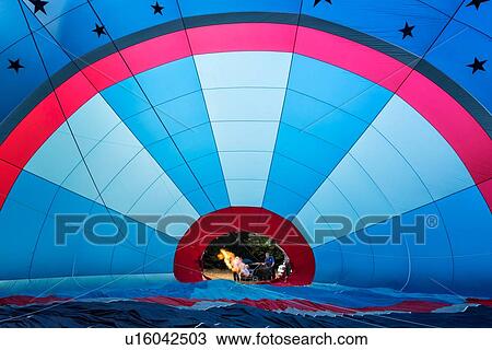 Stock Image - Todi, Italy: July 11, 2013 - Todi Mongolfiere Hot Air Balloon Festival; interior view of red and blue hot air balloon being inflated with people using burner, Umbria, Italy. Fotosearch