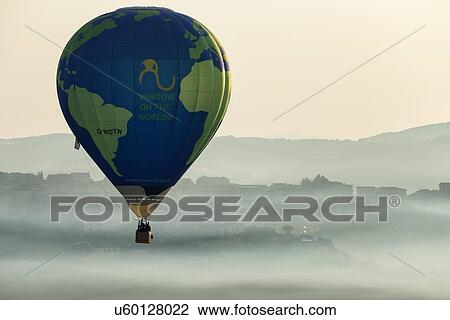 Stock Image - Todi, Italy: July 16 2013; Todi Mongolfiere Hot Air Balloon Festival - blue and green hot air balloon over Middle Tiber Valley with hills layered in early morning hazy sunshine, aerial view, Umbria, Italy. Fotosearch