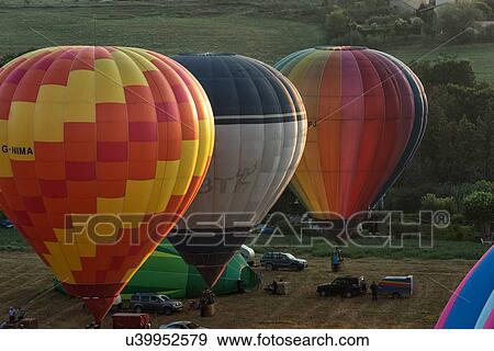 Todi, Italy: July 16 2013; Todi Mongolfiere Hot Air Balloon Festival - hot air balloons inflated, in a row and ready for launch in Middle Tiber Valley field, in early morning sunshine, aerial view, Umbria, Italy View Large Photo Image Stock Photo - Todi, Italy: July 16 2013; Todi Mongolfiere Hot Air Balloon Festival - hot air balloons inflated, in a row and ready for launch in Middle Tiber Valley field, in early morning sunshine, aerial view, Umbria, Italy. Fotosearch