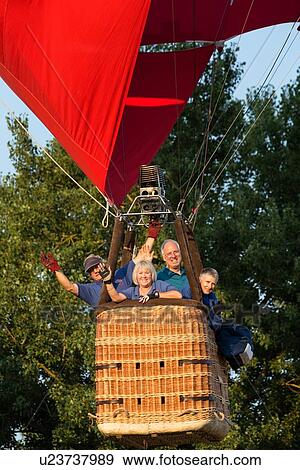 Todi, Italy: July 18, 2013; Todi Mongolfiere Hot Air Balloon Festival - red hot air balloon rising into sky as seen from below, detail view, with passengers waving from basket, tree tops in background in early morning sunshine, Umbria, Italy View Large Photo Image Stock Photo - Todi, Italy: July 18, 2013; Todi Mongolfiere Hot Air Balloon Festival - red hot air balloon rising into sky as seen from below, detail view, with passengers waving from basket, tree tops in background in early morning sunshine, Umbria, Italy. Fotosearch