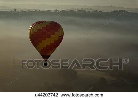 Todi Mongolfiere Hot Air Balloon Festival - orange and yellow hot air balloon over Middle Tiber Valley with hills layered in early morning hazy sunshine, Umbria, Italy View Large Photo Image Stock Image - Todi Mongolfiere Hot Air Balloon Festival - orange and yellow hot air balloon over Middle Tiber Valley with hills layered in early morning hazy sunshine, Umbria, Italy. Fotosearch