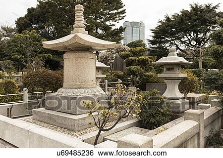 Stock Photograph - Tokyo, Japan: March 2, 2013 - Japanese gravestones in cemetery with beautiful surrounding landscaping of trees and bushes, in spring, Tokyo, Japan. Fotosearch