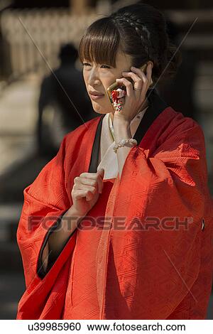 Stock Image - Tokyo, Japan: March 2, 2013 - Traditional Japanese wedding: portrait of guest closeup, showing traditional costume as she talks on modern cellphone, Shinto Mehji shrine, Tokyo, Japan. Fotosearch
