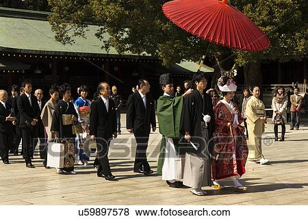 Stock Photo - Tokyo, Japan: March 2, 2013 - Traditional Japanese wedding procession with bride and groom covered by red umbrella, relatives walking behind in central area of Shinto Mehji shrine, Tokyo, Japan. Fotosearch